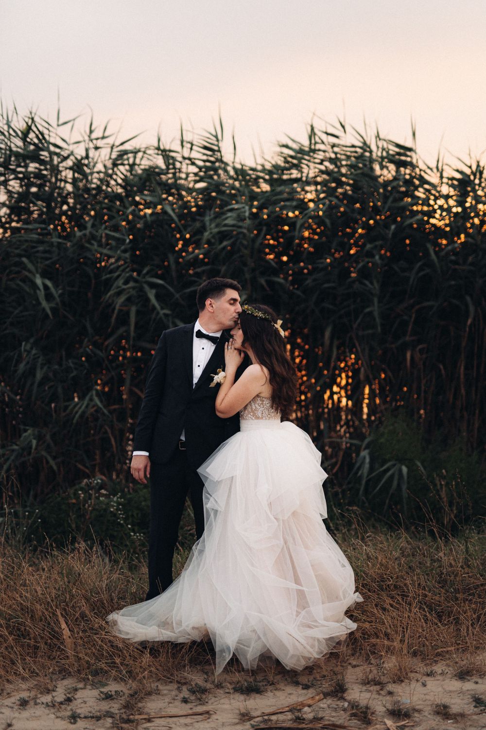 Romantic wedding portrait against tall reeds backlit by golden sunset.