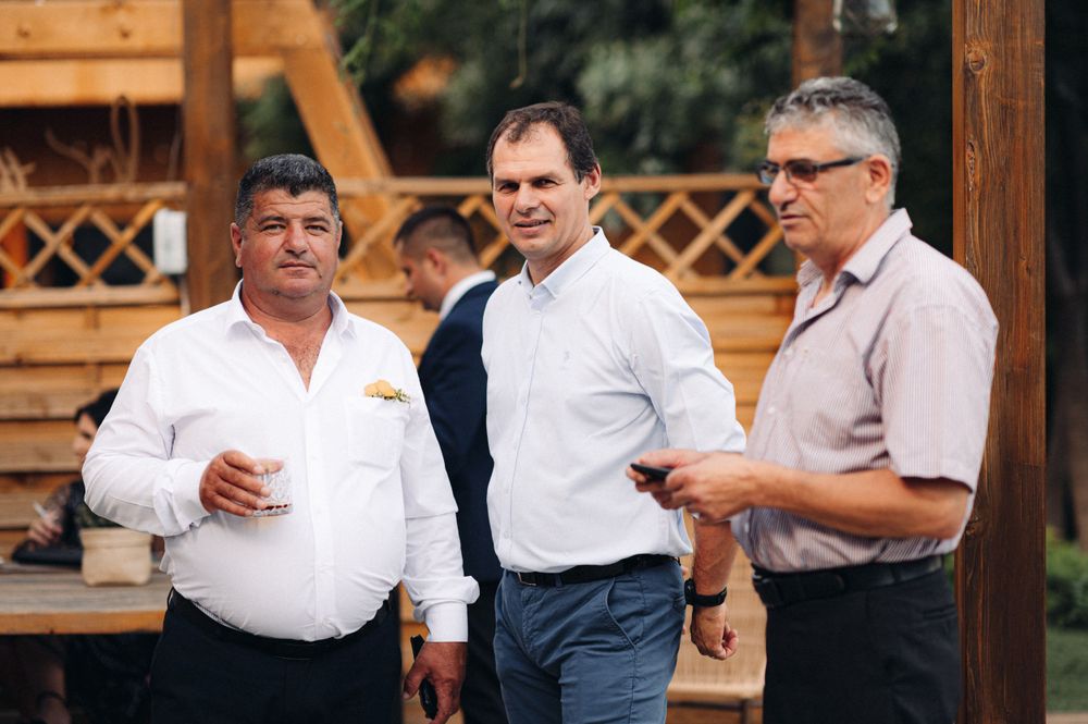Three guests chatting during outdoor gathering near wooden pavilion.