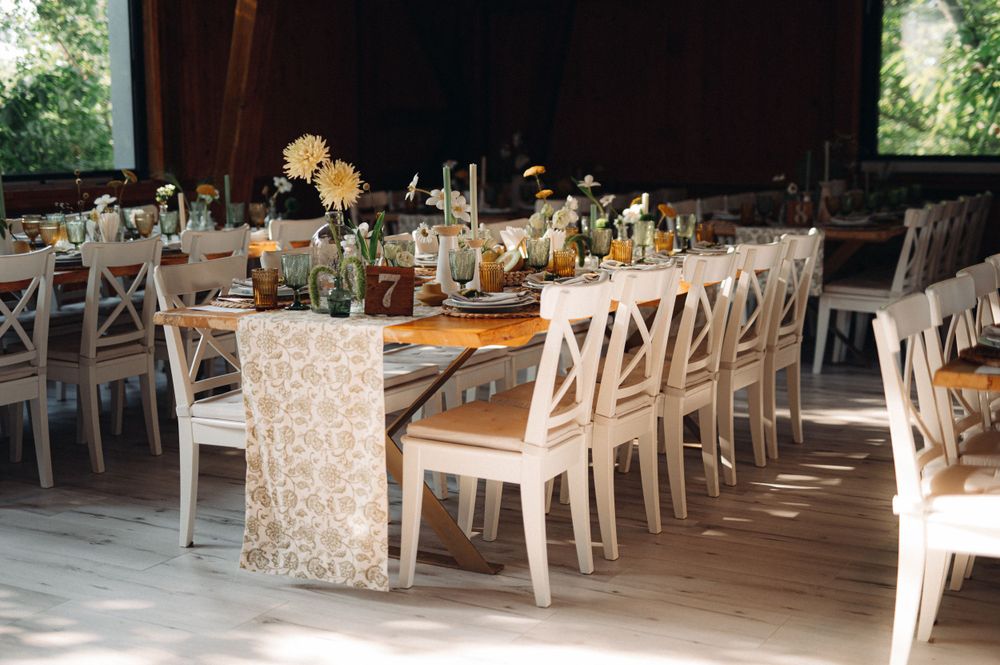 Rustic wedding reception table setup with white crossback chairs and floral centerpieces in a barn venue.