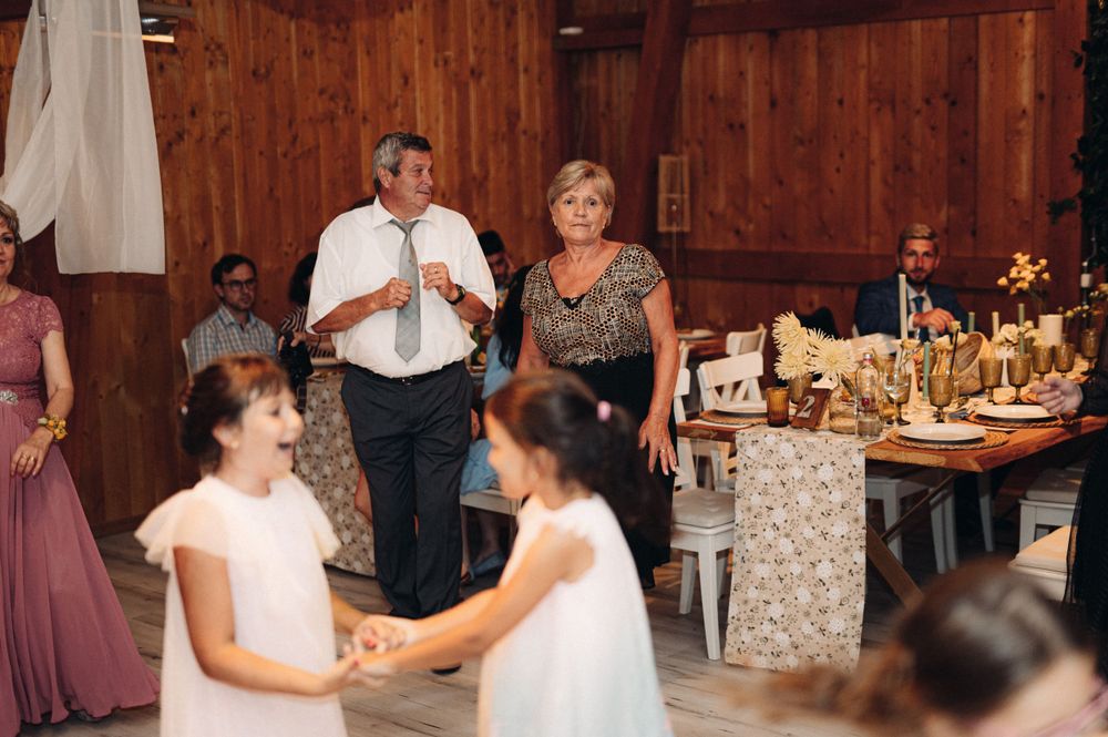 Wedding guests dancing and celebrating in a rustic wooden venue with decorated tables.