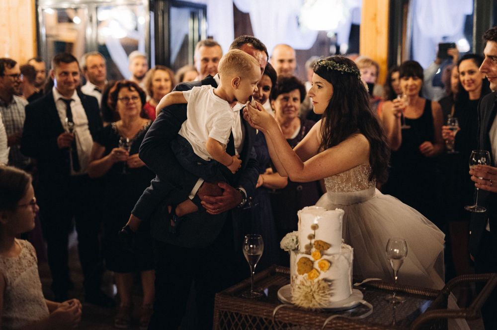 Wedding cake cutting moment surrounded by guests during evening reception celebrations.