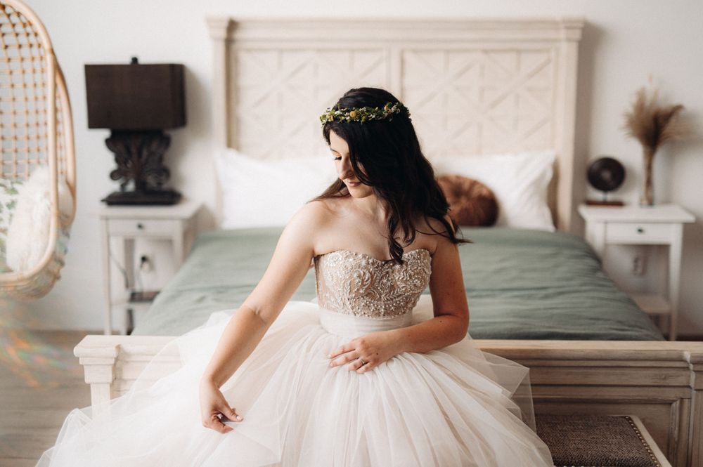 Romantic bridal portrait with flowing tulle skirt against textured headboard and hanging rattan chair.