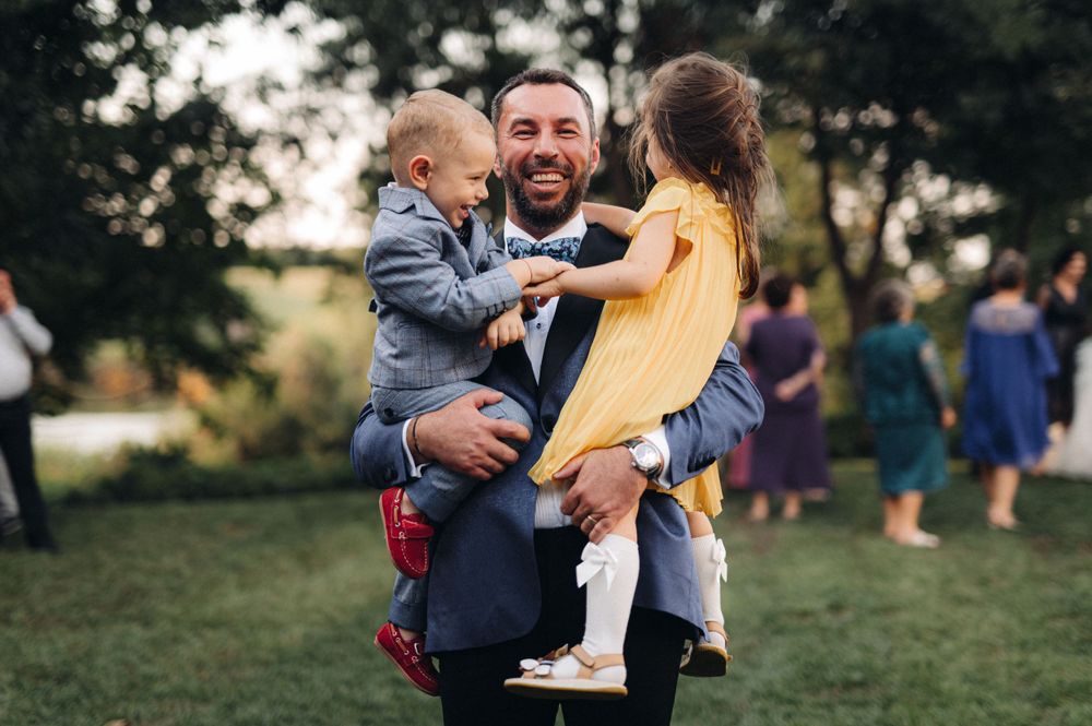 Family shares joyful moment outdoors at social gathering on grassy lawn with other guests in background.