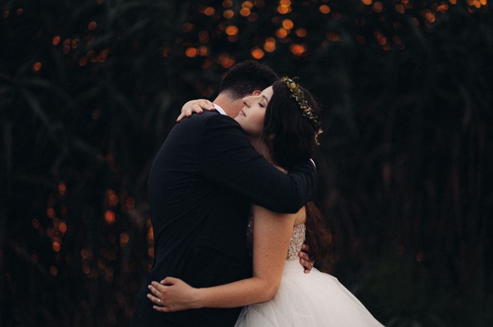 Intimate embrace captured against bokeh lights and dark foliage.