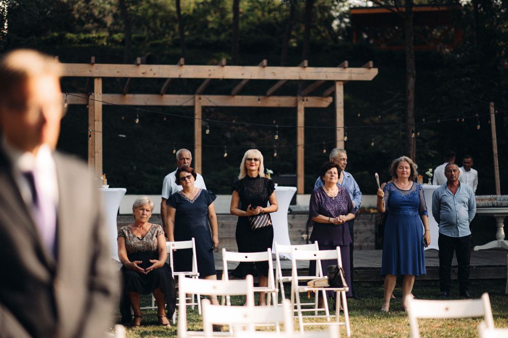 Wedding guests in blue dresses standing near white chairs at outdoor ceremony setup.