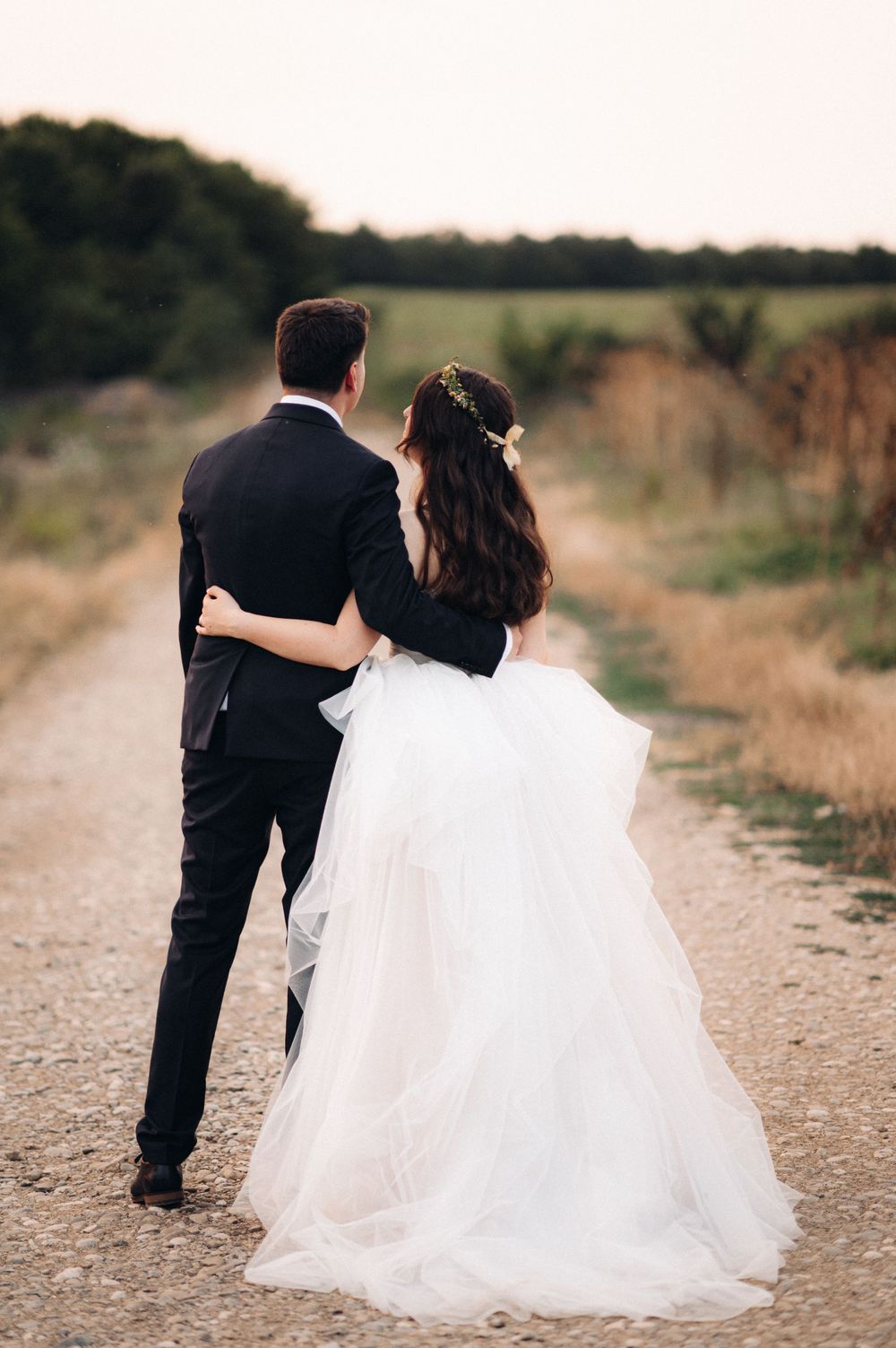 Couple walking arm in arm down a country path, bride's white dress flowing behind them.