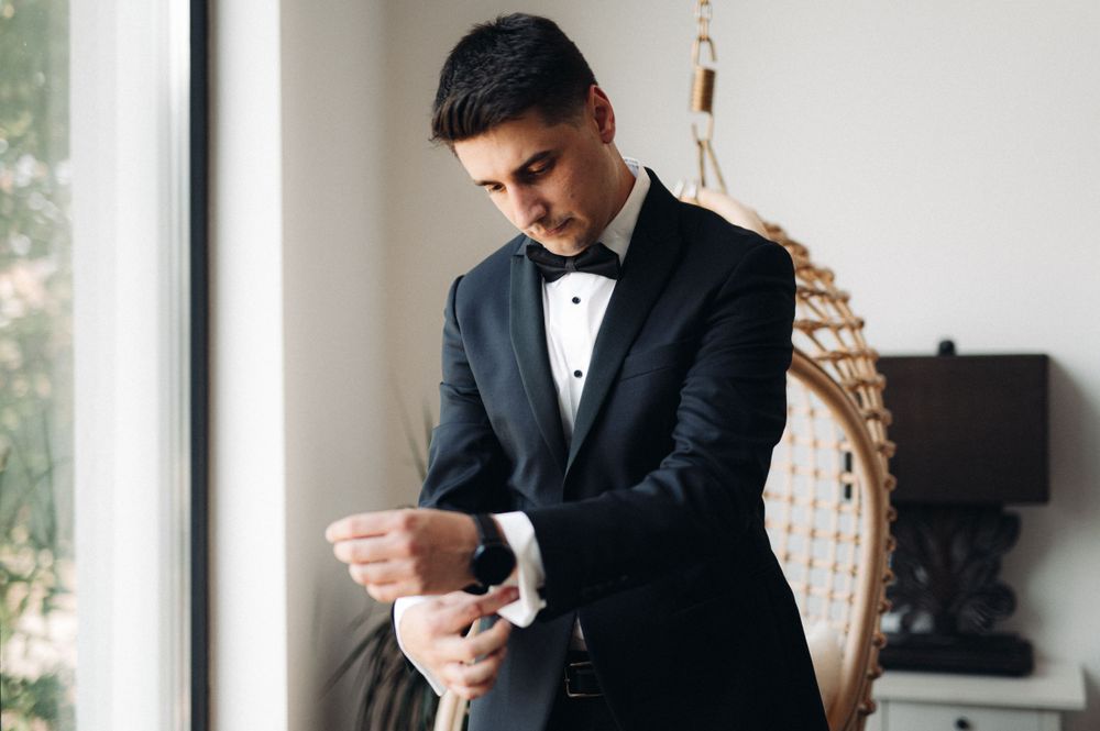 A black tuxedo jacket being adjusted while standing by a window.