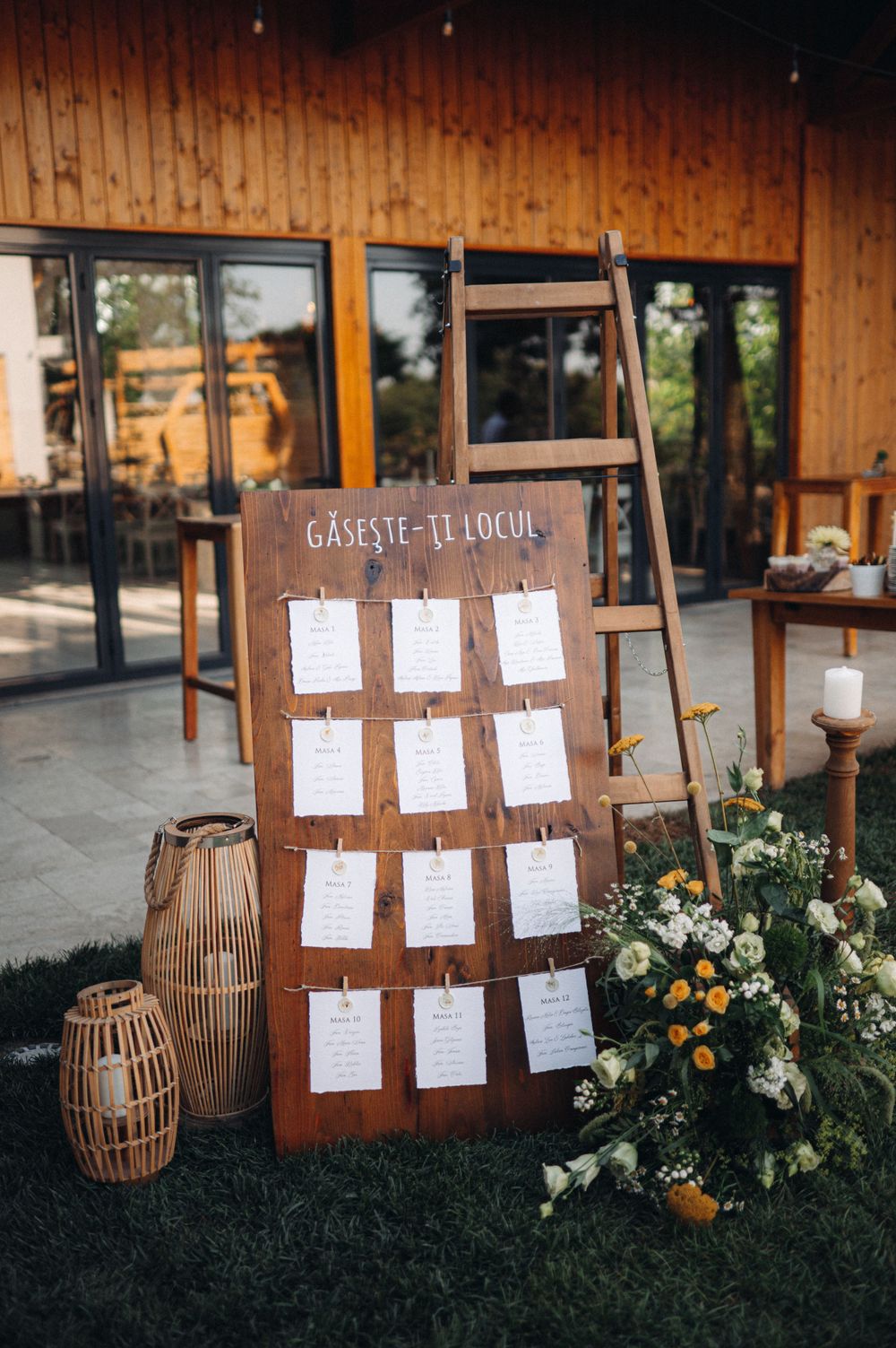 A wooden seating chart display board decorated with floral arrangements and lanterns.