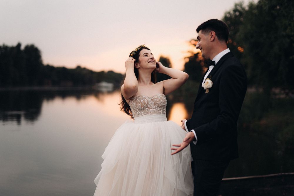 Candid moment between newlyweds laughing by the lake during sunset.