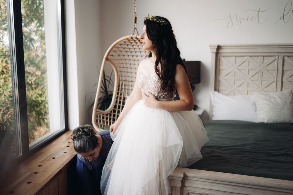 A dreamy bridal portrait featuring an elegant strapless wedding gown and a bohemian hanging rattan chair by a window.