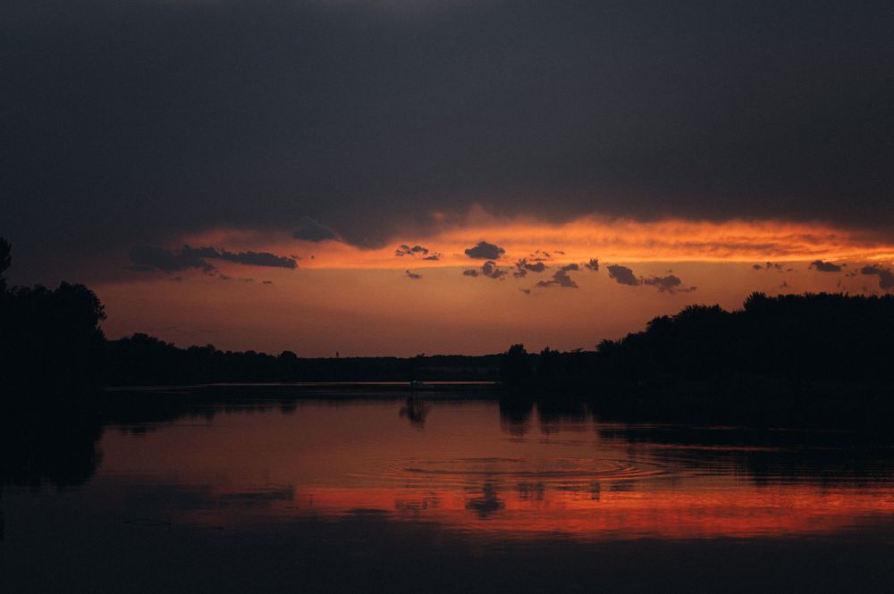 Dramatic orange sunset over a lake with silhouetted trees and reflective waters.