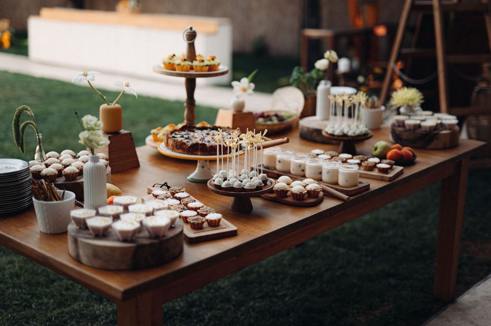 An elegant dessert table with cupcakes, cake pops and various sweet treats arranged on a wooden surface outdoors.