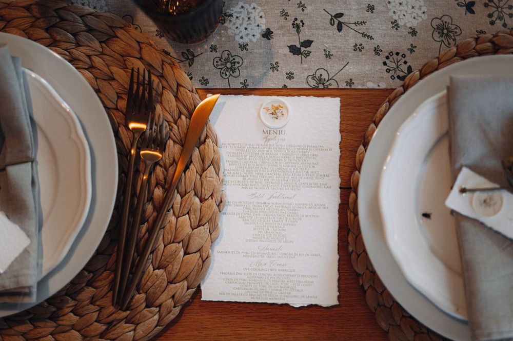 A wedding menu card placed between elegant white place settings on a woven placemat.