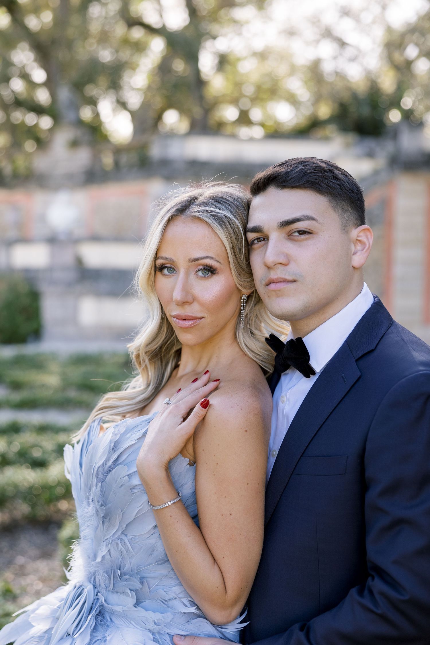 A couple in formal attire poses together against a garden backdrop.