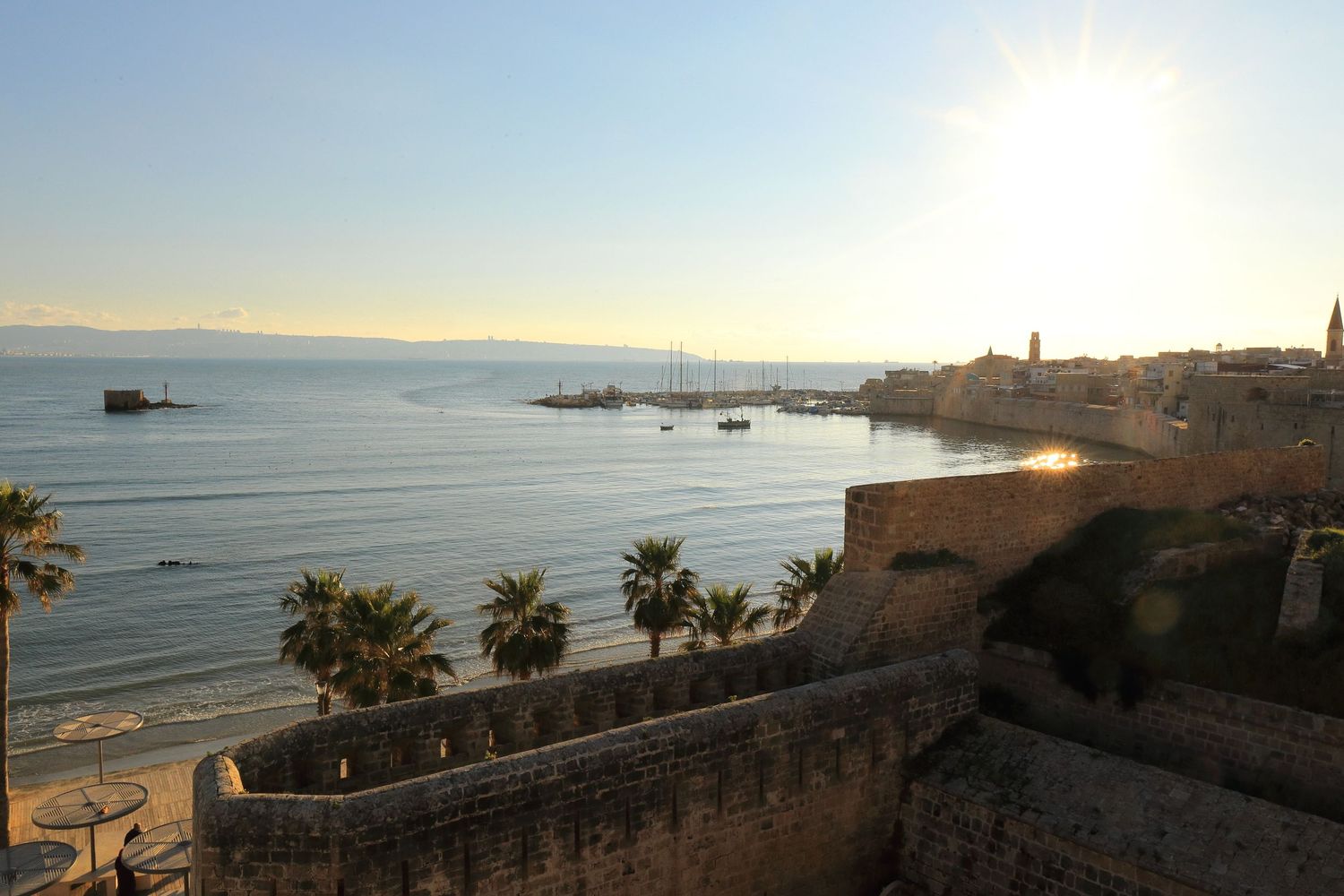 Panoramic coastal view of Mediterranean shoreline with historic fortress walls at sunset.