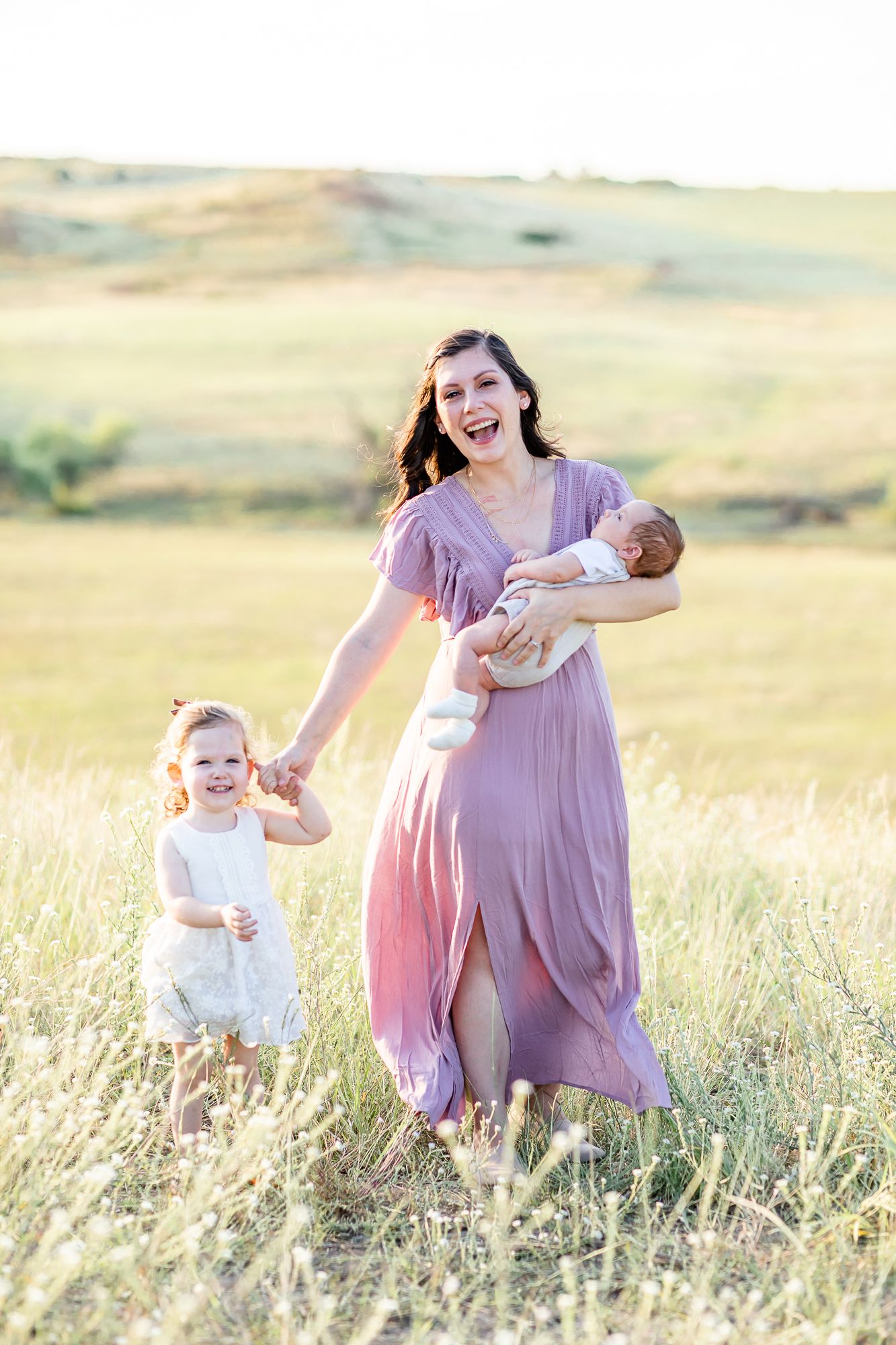 Mom snuggles her baby boy and holds her toddler girl's hand as they walk through the meadow in Larkspur, Colorado.