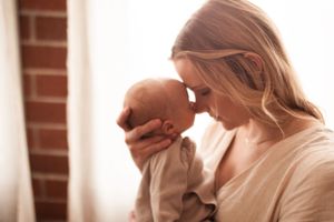 Warm intimate moment between parent and baby near window with brick wall.