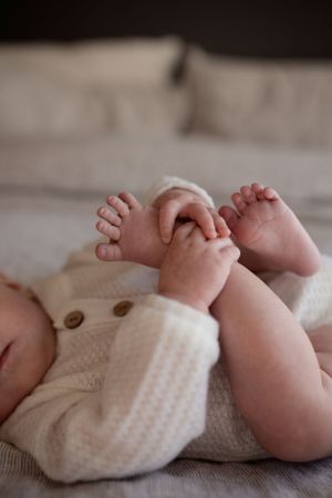 Close up of baby feet in white knit clothing against neutral bedding.