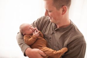 A tender moment between parent and infant wearing a brown onesie against a light background.
