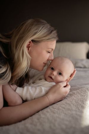 Intimate moment between parent and baby lying together on cream colored bedding.