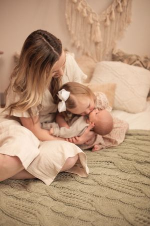 A tender family moment on a cozy knit blanket with a baby and decorative macrame wall hanging in the background.