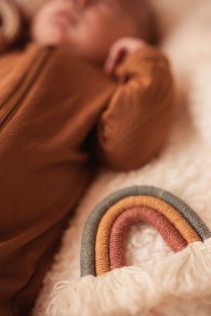 Close-up of a brown sleeper with a rainbow decorative element against a soft textured background.
