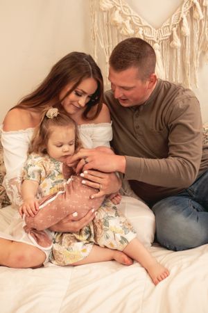 A loving family moment captured on a bed with macrame wall decor in warm neutral tones.