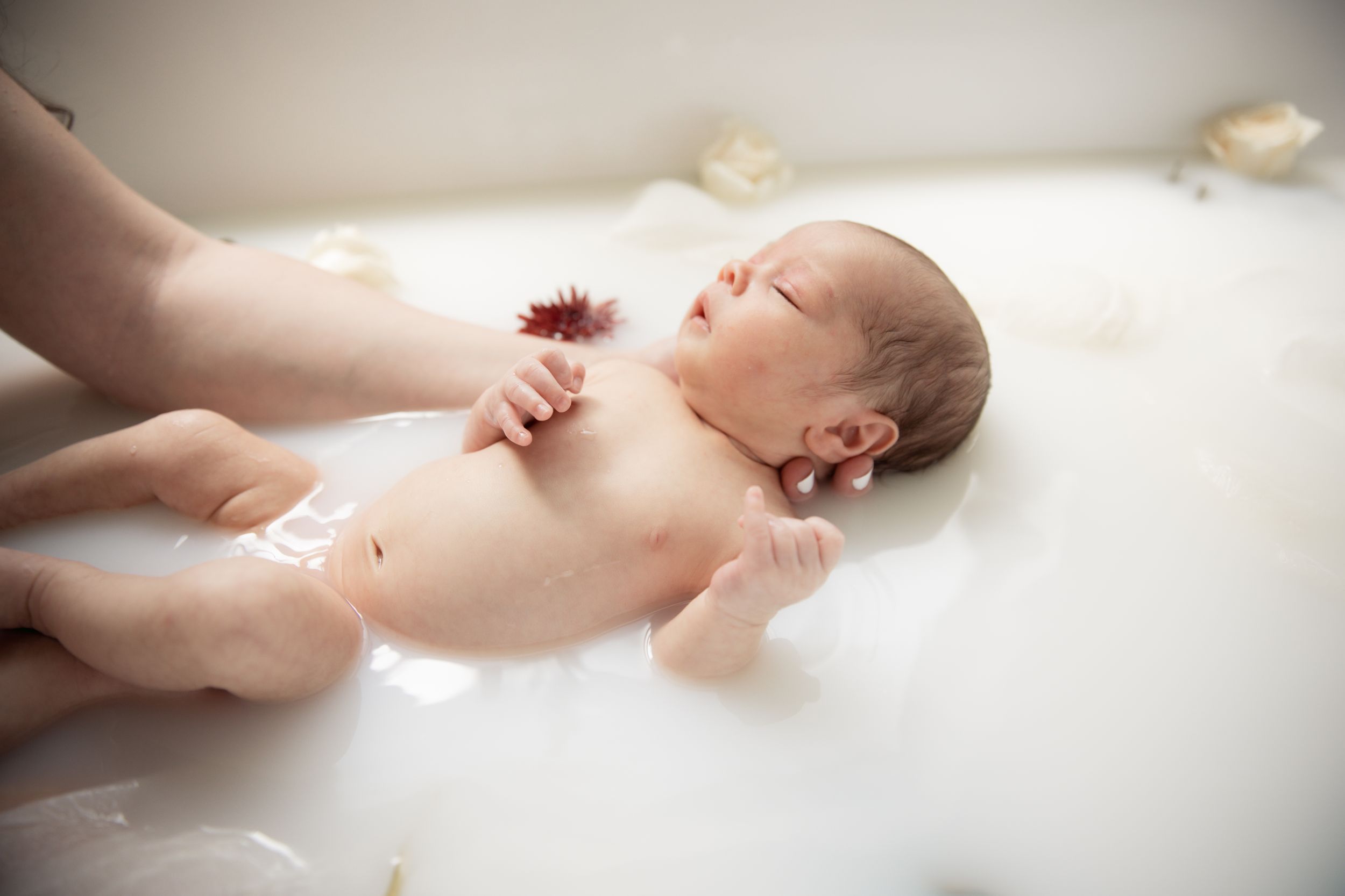 A newborn baby lying peacefully on white fabric during a photography session.