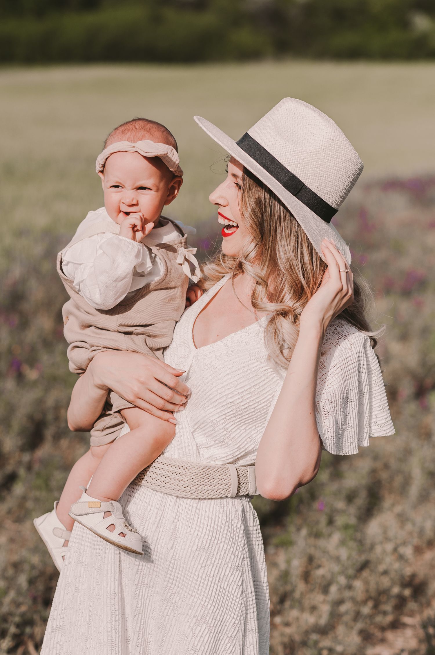 Mother and baby share joyful moment in field wearing white summer outfits.