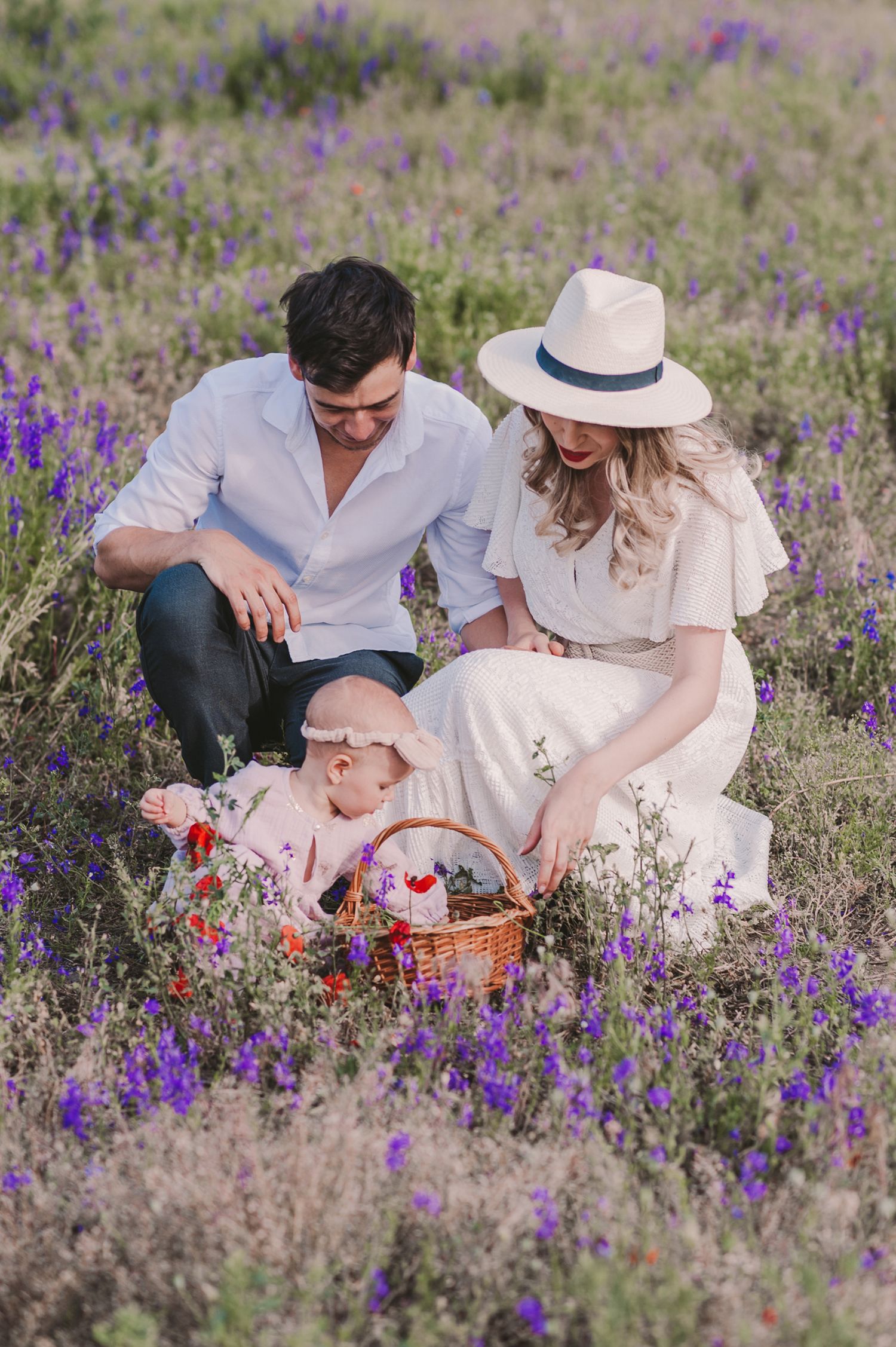 Family relaxing on blanket amid purple wildflowers and red poppies.