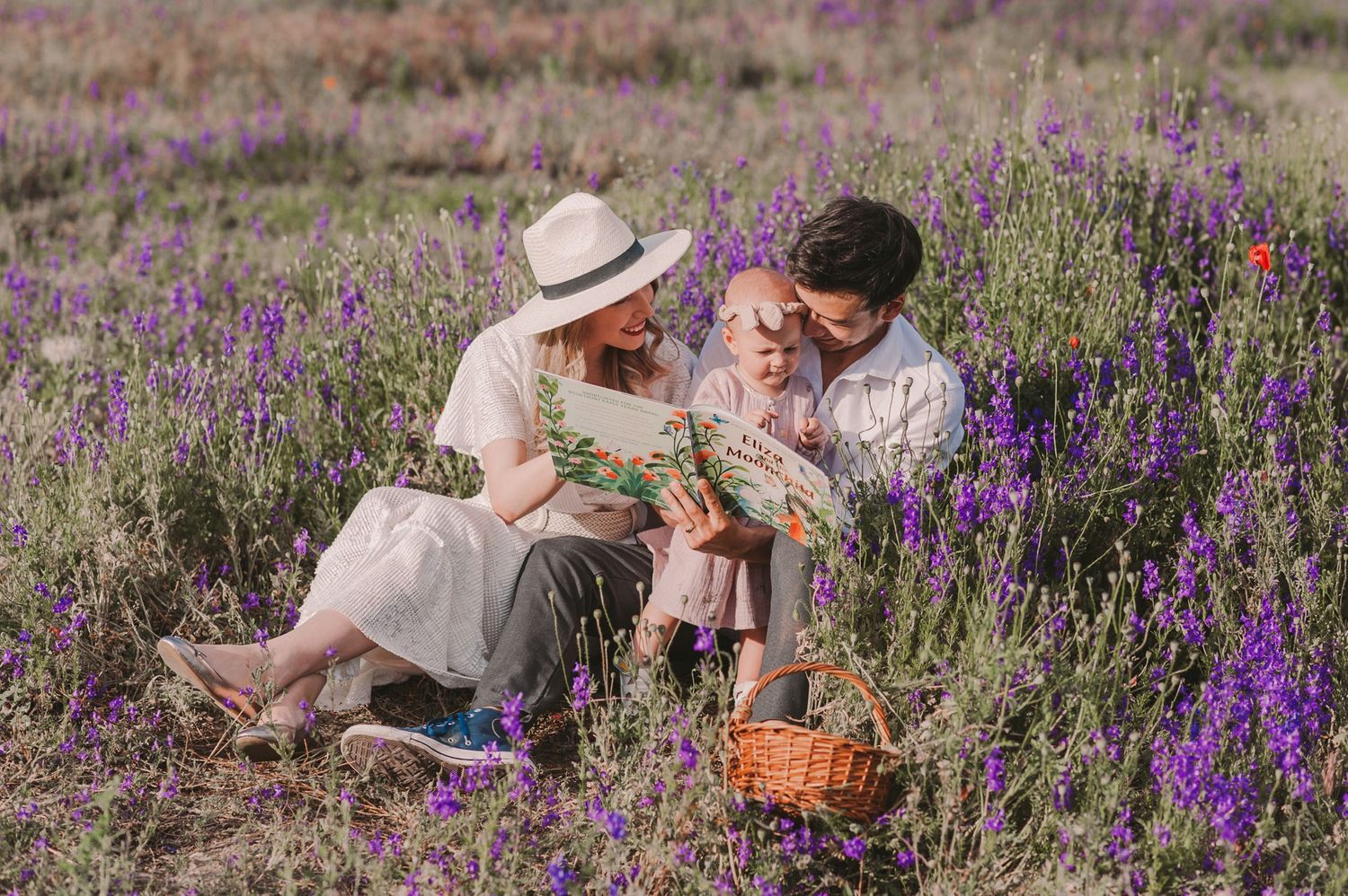 Figures in light summer attire relax in a field of blooming purple and red wildflowers.