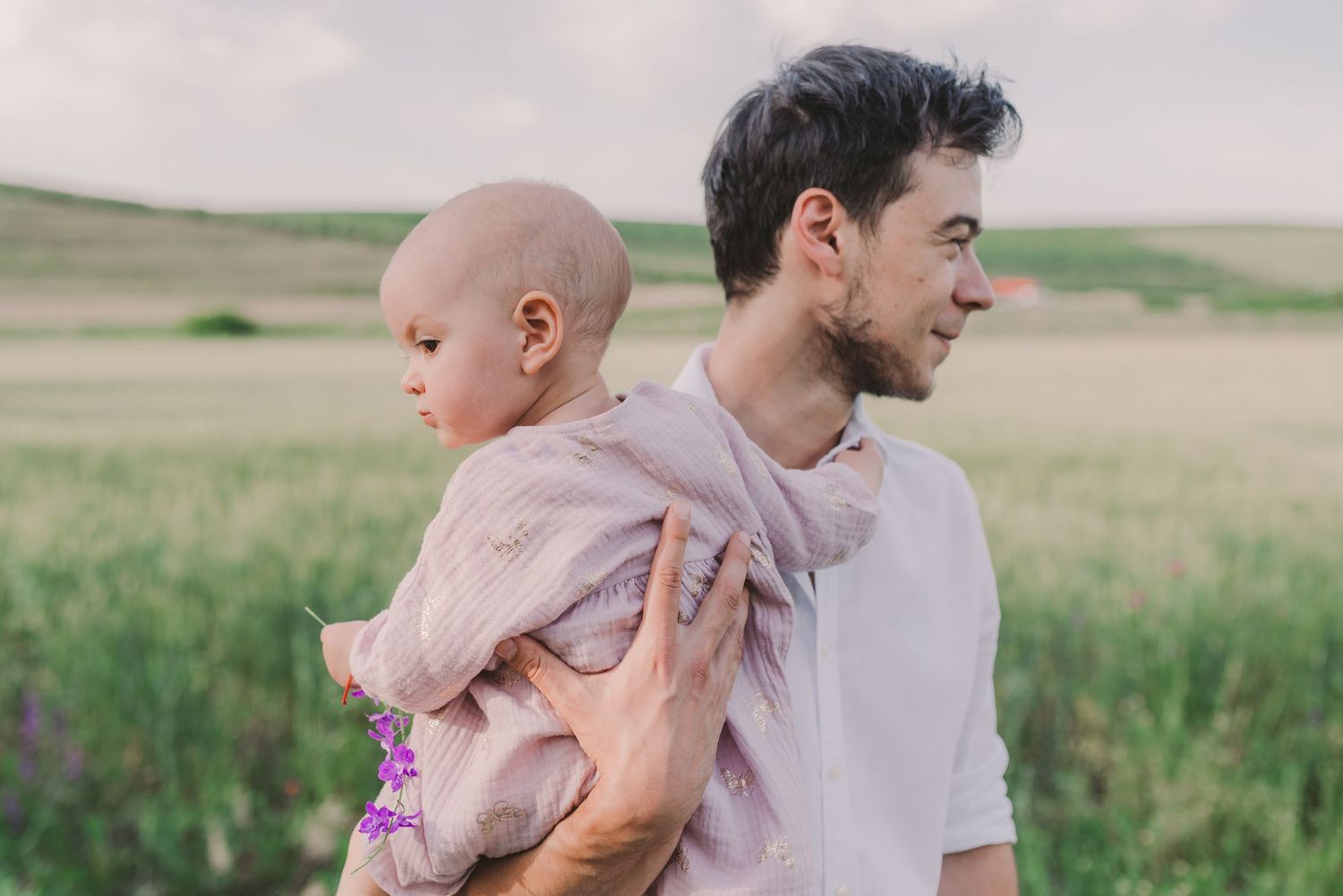 Family enjoying a tender moment together in a sunlit meadow with tall grass and trees in the background.