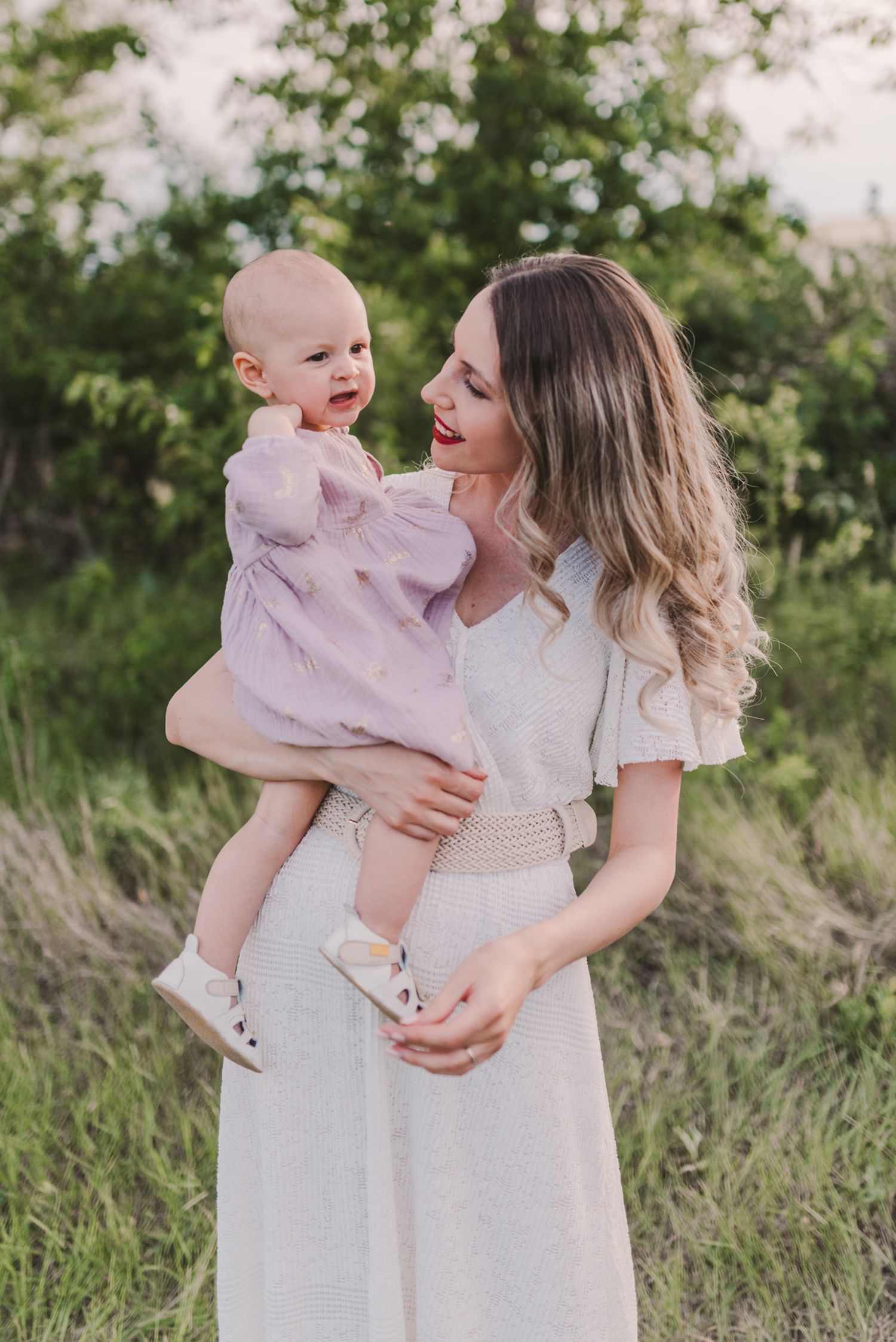 Parent and child wearing white dresses share joyful moments in a grassy field during golden hour.