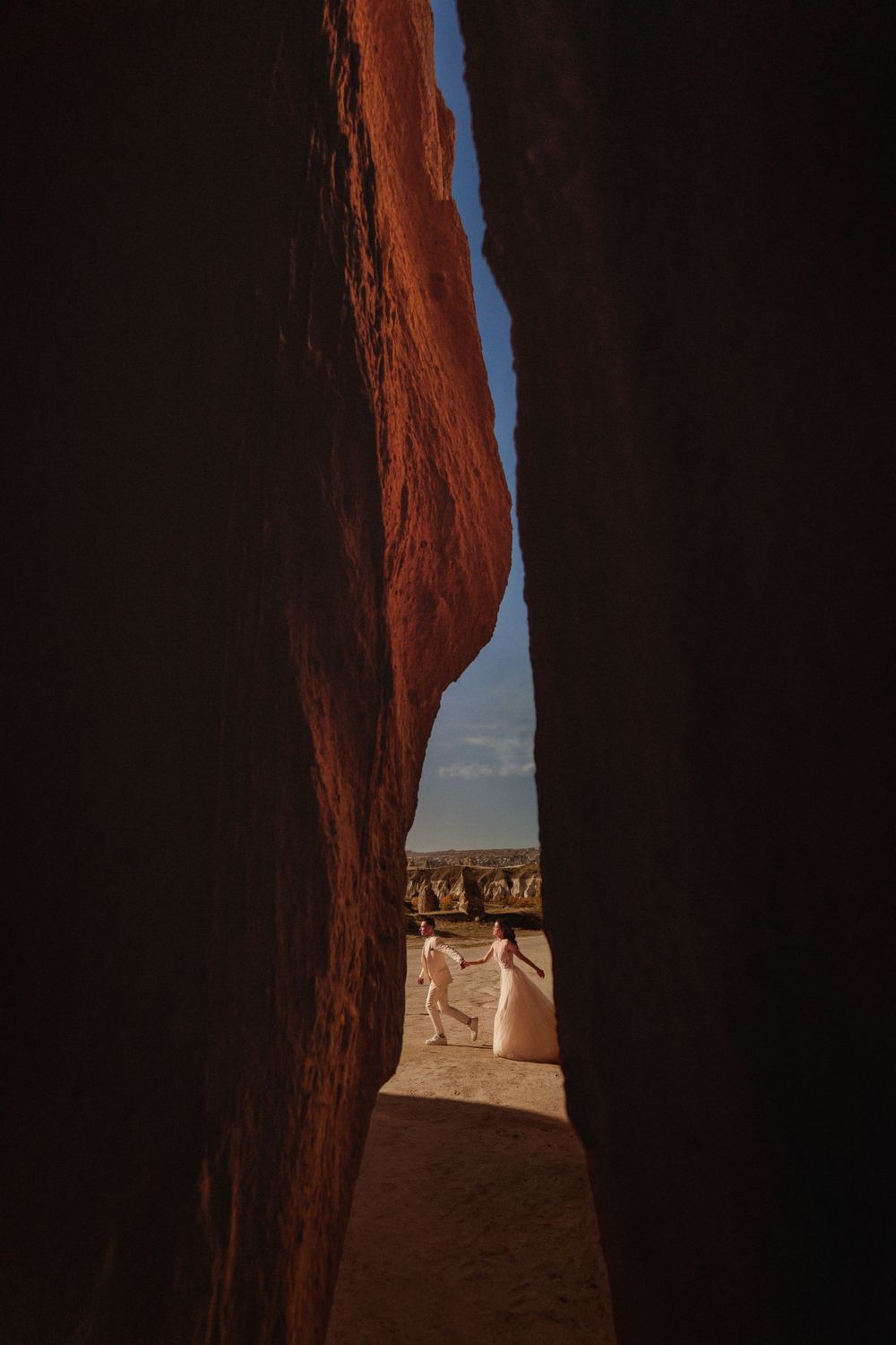 View through a narrow red rock canyon opening to a desert landscape beyond.