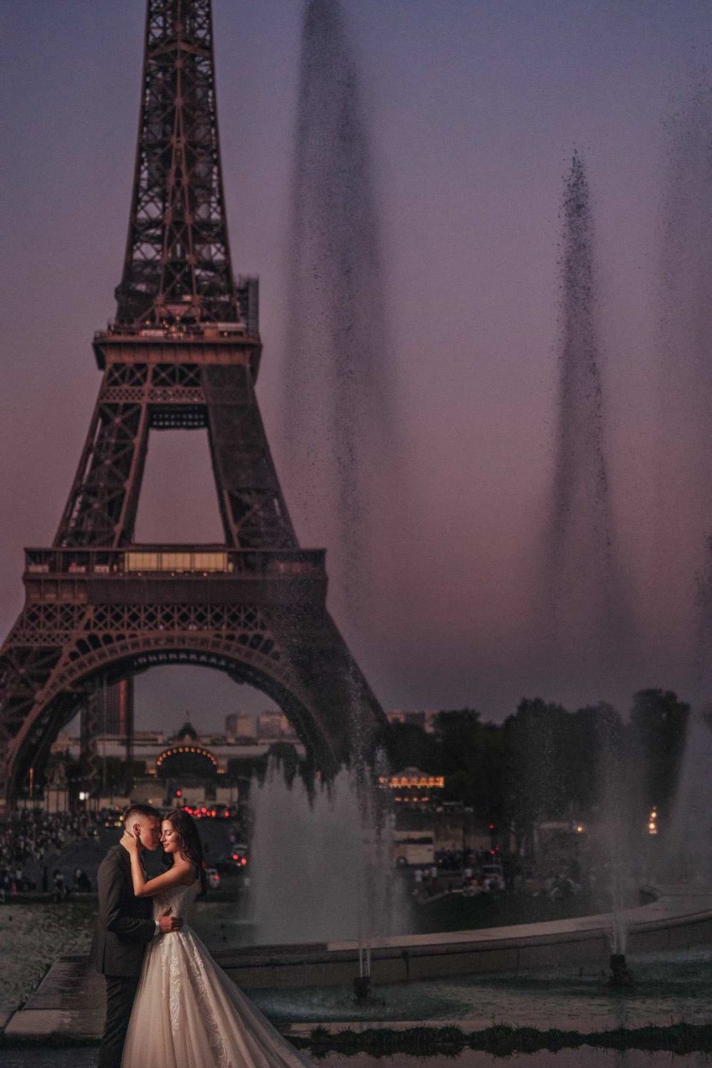 Romantic scene at the Eiffel Tower with fountains and soft purple dusk lighting.