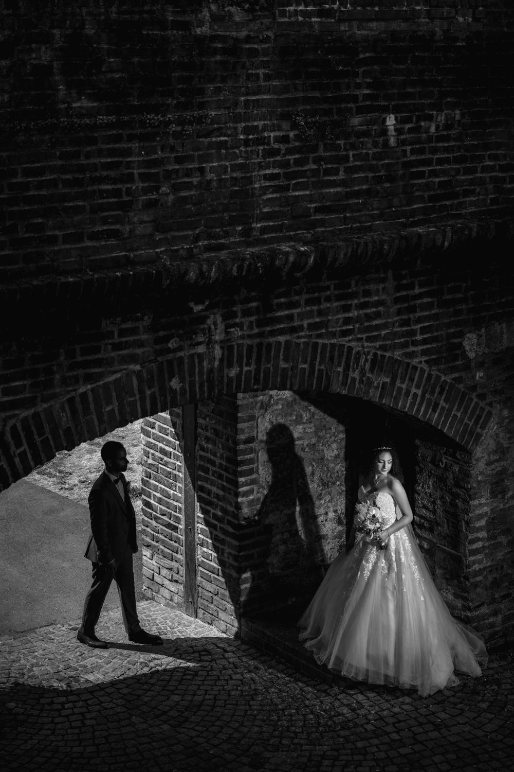 Dramatic wedding photography in brick tunnel with artistic lighting and shadows.