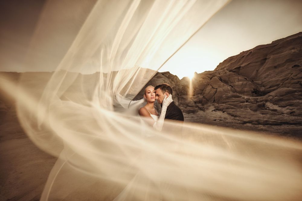Flowing white bridal veil against dramatic rocky landscape at sunset.