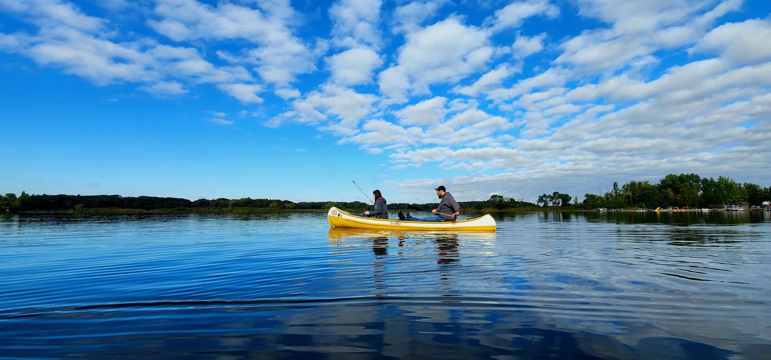 Yellow canoe on calm blue lake water under wispy cloud-filled sky.