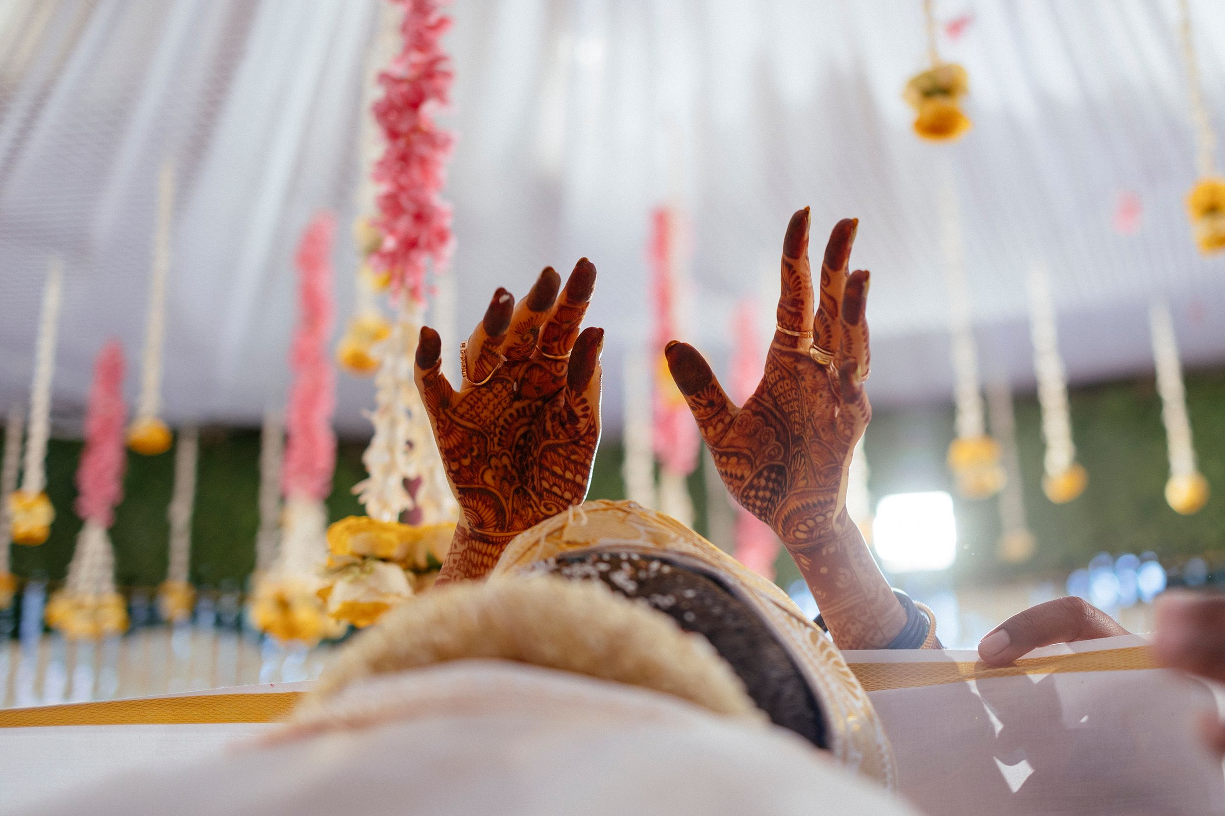 Decorated hands with intricate henna designs raised during an Indian wedding ceremony.