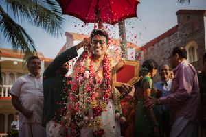 A South Indian traditio wedding with flower petals being showered on the groom under a red umbrella during Kasi Yatra.