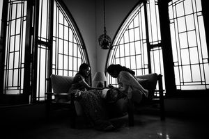 Artistic silhouette of couple seated by arched windows in dramatic black and white composition of applying Mehendi.