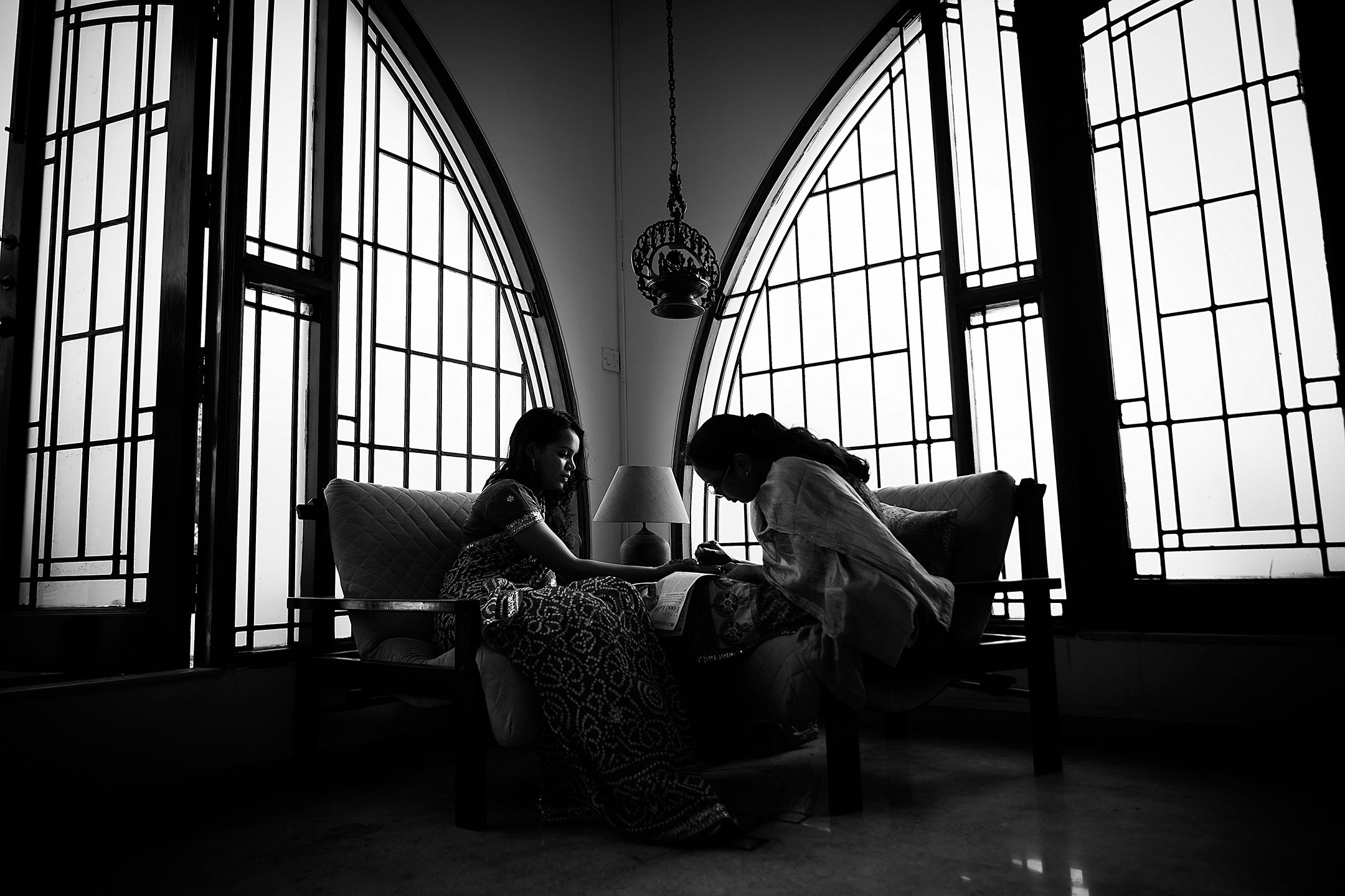 Artistic silhouette of couple seated by arched windows in dramatic black and white composition of applying Mehendi.