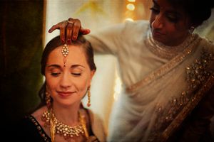 Close-up of traditional Indian bridal preparation with jewelry and bindi application.