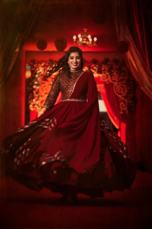 Bride twirling in flowing red dress against dramatic red-lit backdrop.