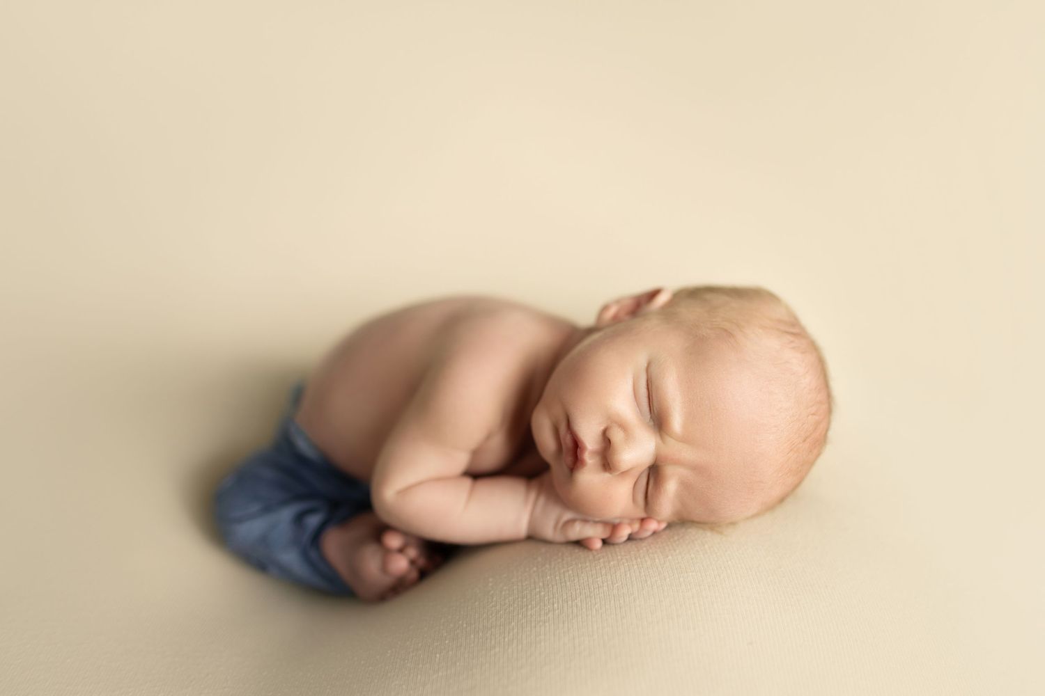 Simple minimalist newborn portrait against cream colored background.