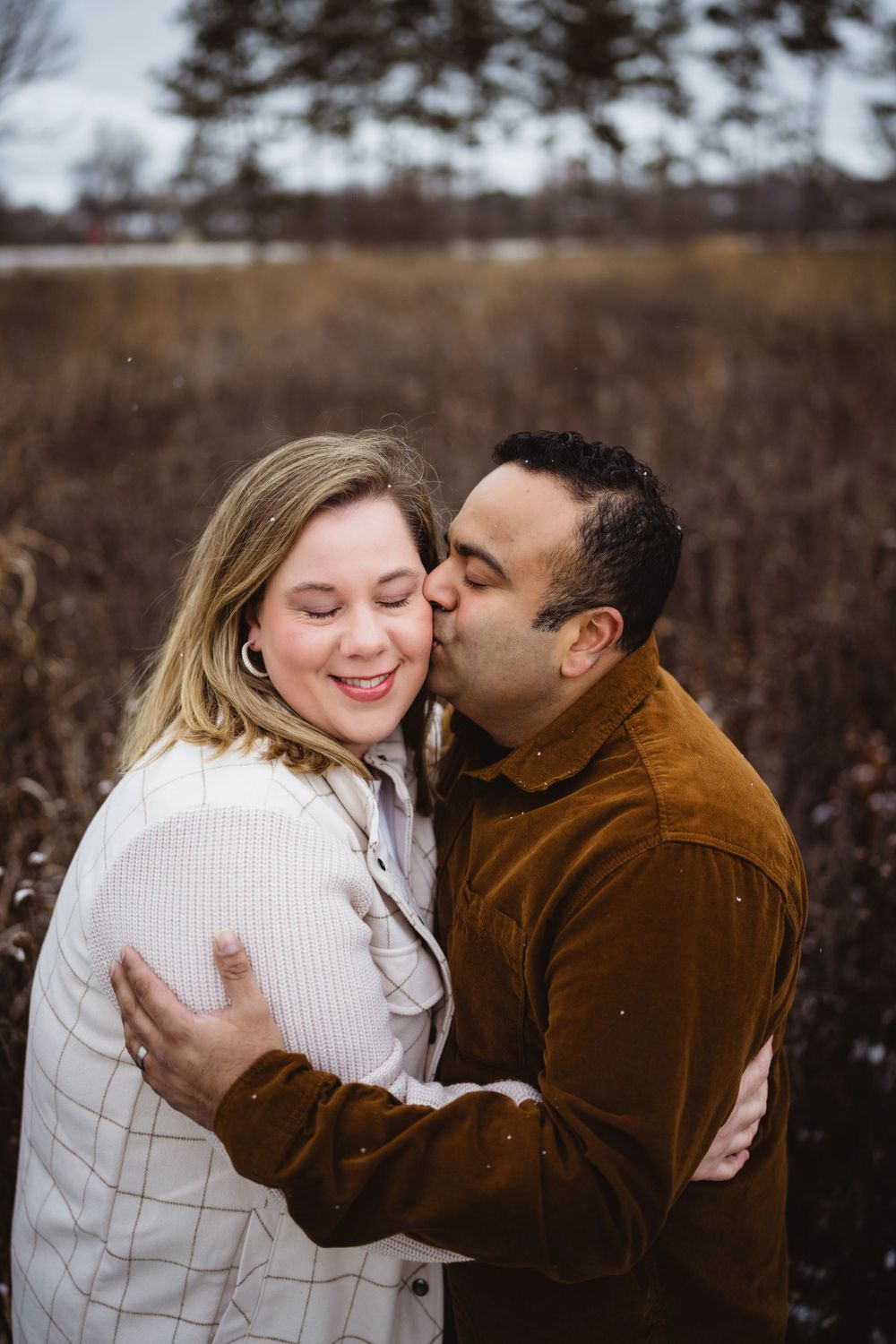 A romantic couple sharing an intimate moment in a winter field setting.