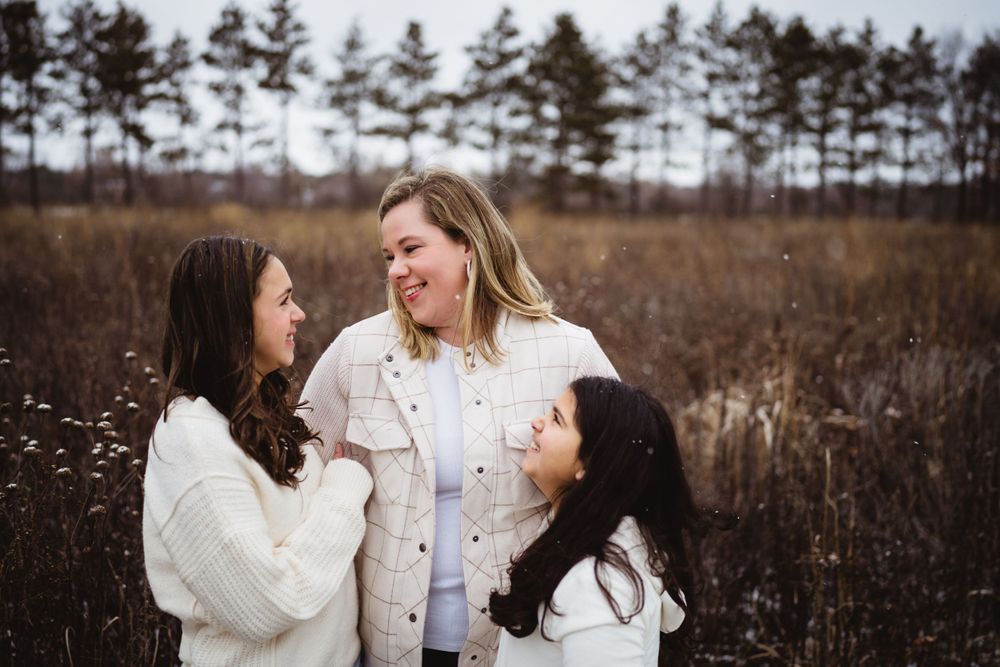 Three people sharing a joyful moment together in a winter field setting.