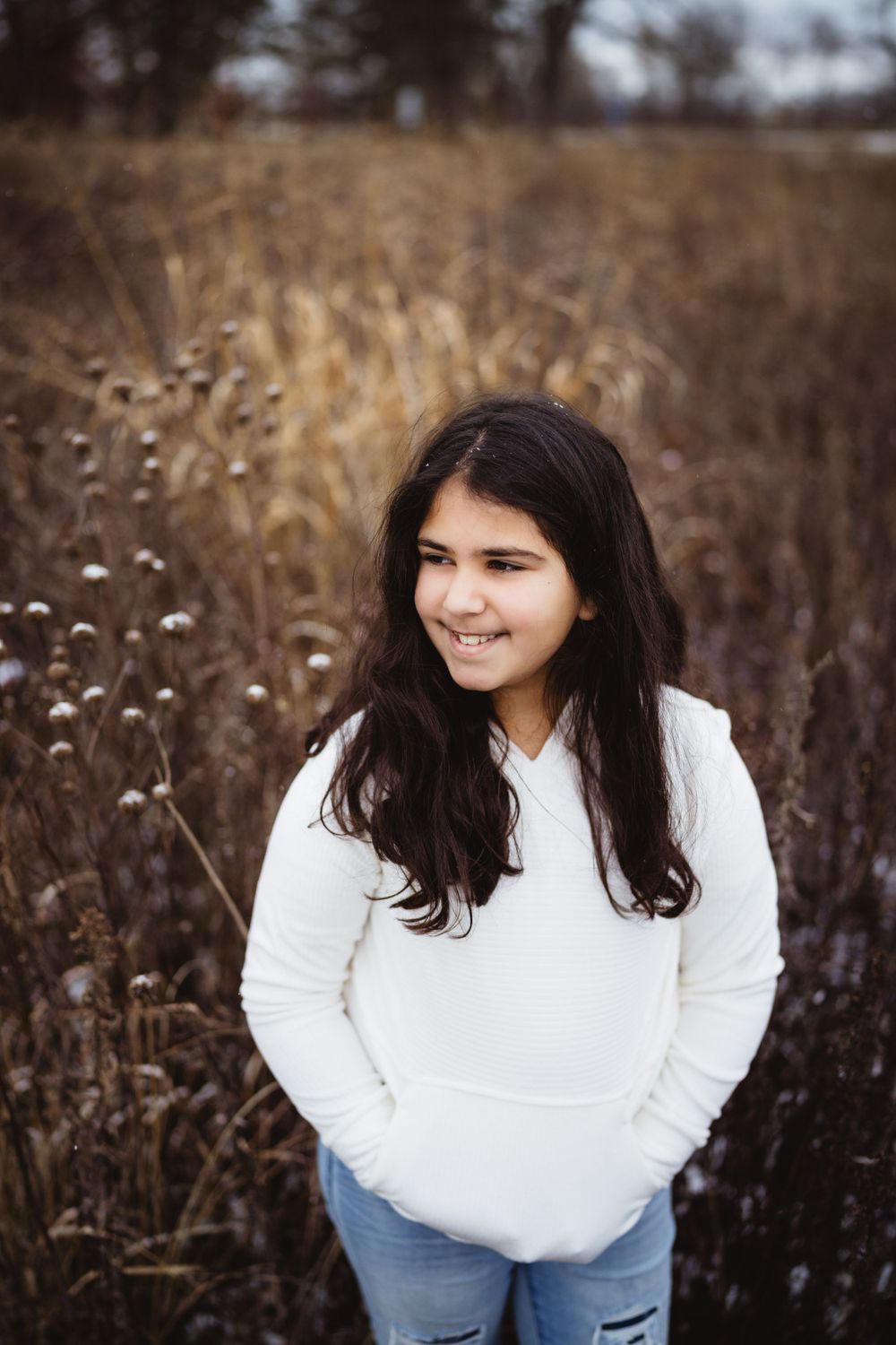 Portrait in a winter field showing someone in a white hoodie smiling warmly.