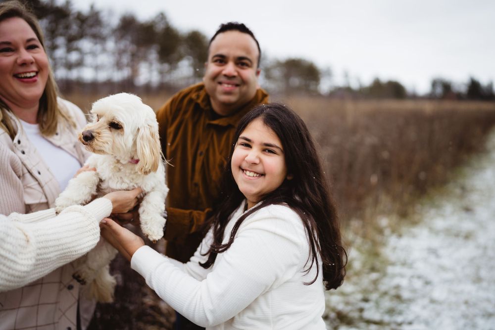 A happy family and their small white dog posing together in a snowy winter field.