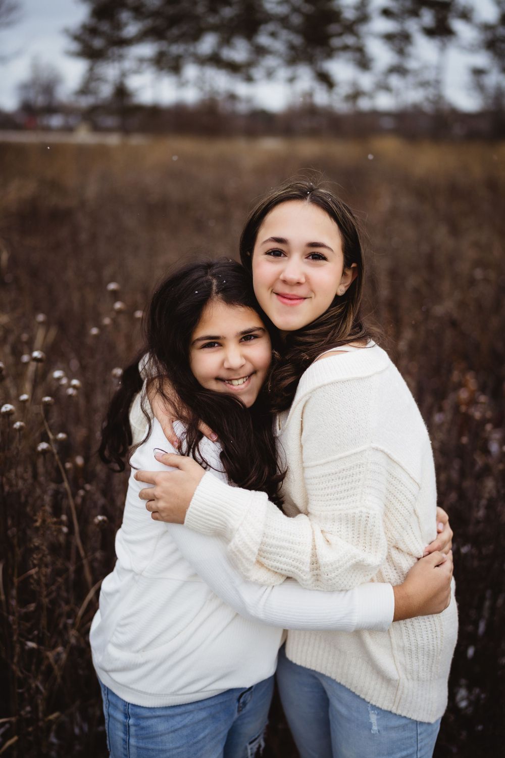 Two people in white sweaters sharing a warm embrace in a winter field setting.
